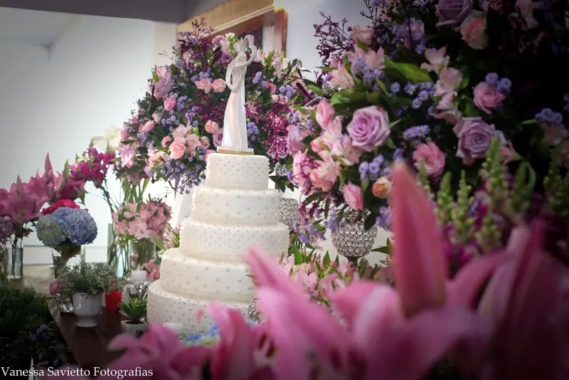 Bolo branco cercado de flores rosa e lilás
