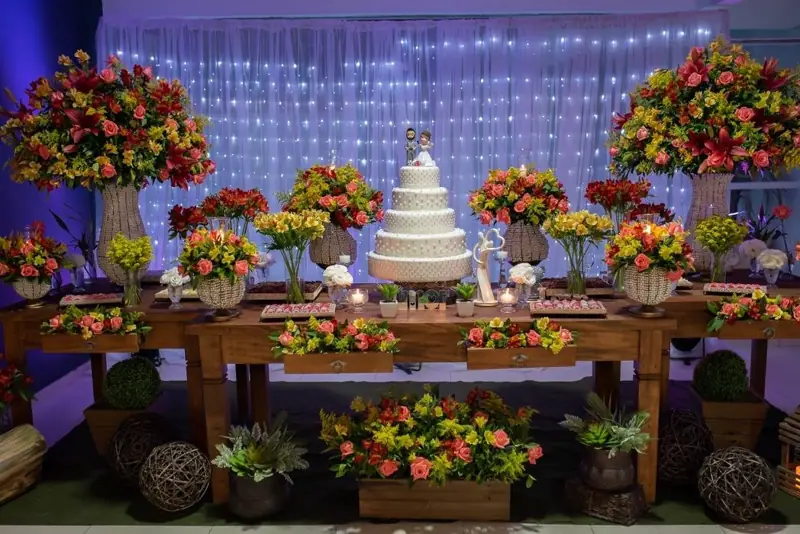 Mesa do bolo decorada com flores naturais vermelhas e laranja
