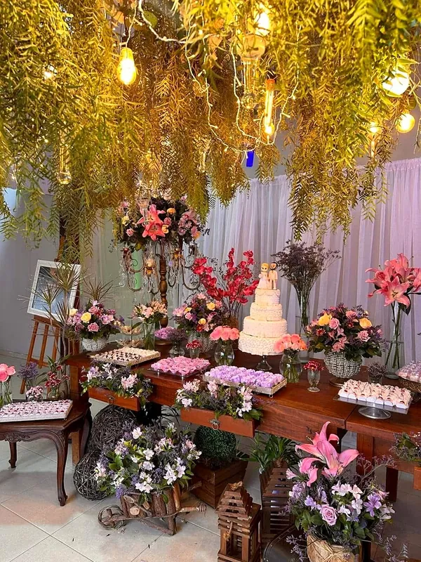 Mesa do bolo e dos doces sob um jardim suspenso de folhagens e luzes