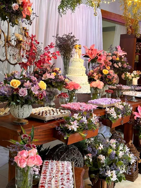 Mesa de doces com bolo branco de vários andares e arranjos de flores naturais