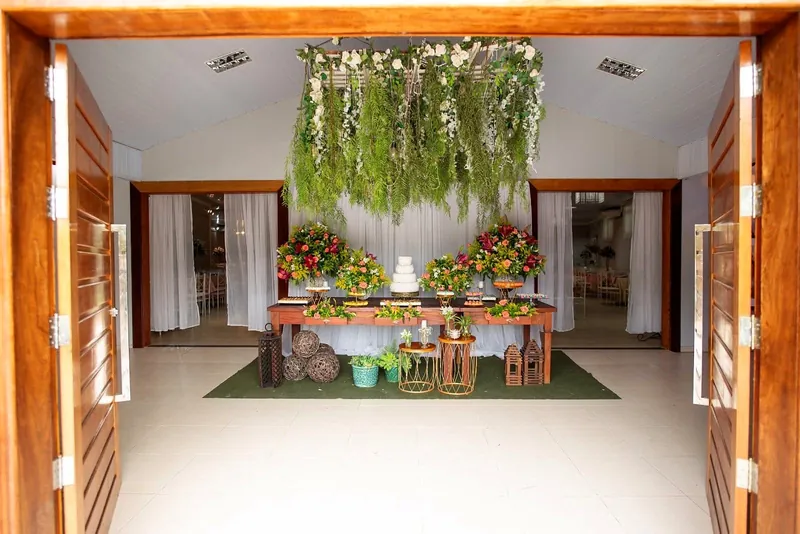 Portas de madeira abertas para o Salão Ouro, com a mesa do bolo decorada com flores e o jardim suspenso